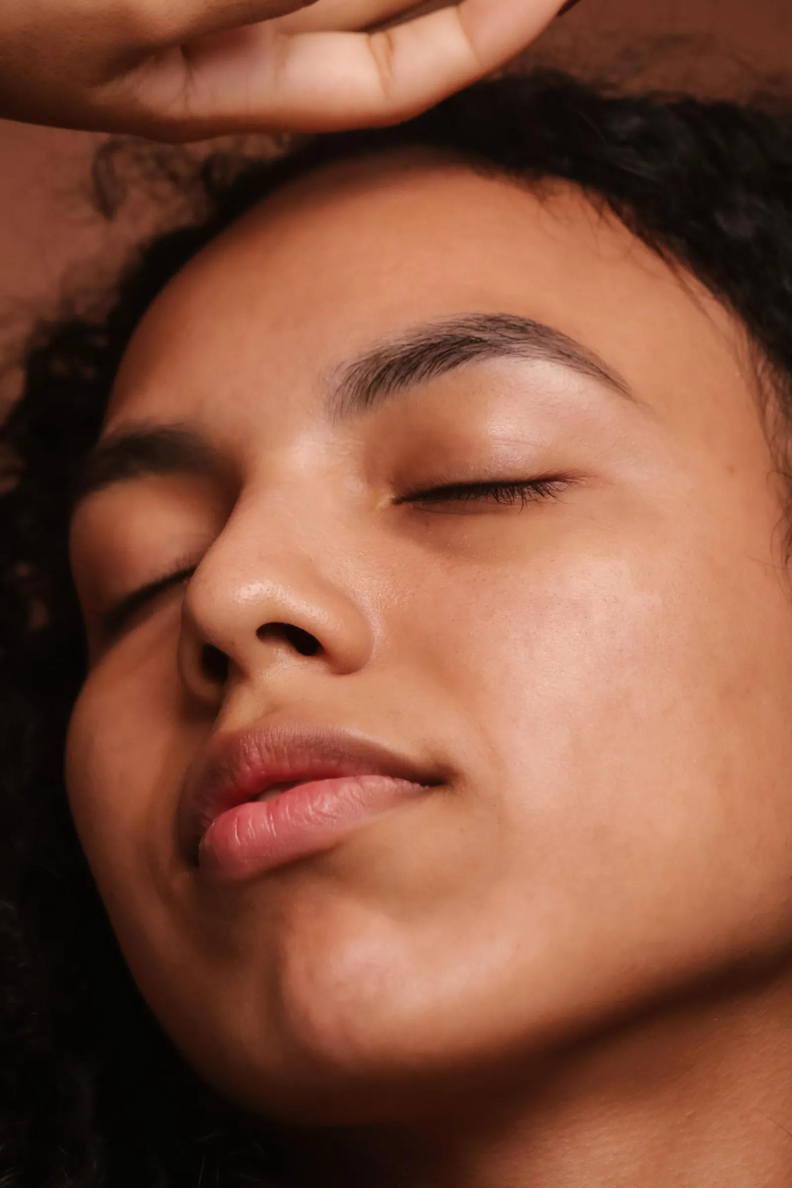A face in warm light, eyes closed, a hand resting on the forehead