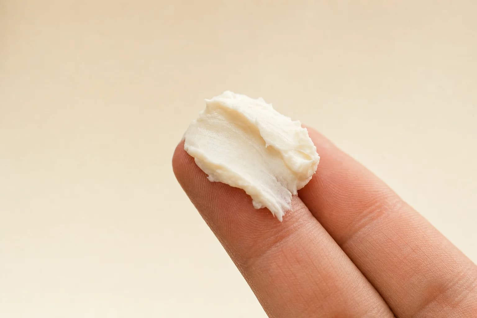 A fingertip of pale botanical cream, thick and matte, held against a warm neutral background
