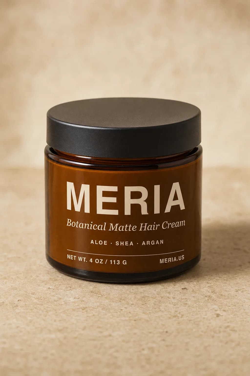 A closed jar of Meria Botanical Matte Hair Cream standing on a warm tan surface.